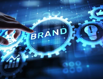 Eine Hand berührt eine holografische Anordnung blauer Zahnräder, im Zentrum steht das Wort BRAND.