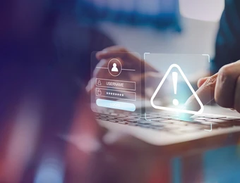 Hände tippen auf Laptop; holografische Sicherheitsanzeige mit Warndreieck und Login-Feldern.