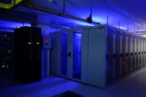 Serverraum mit blauer Beleuchtung, Reihen von Serverracks; links eine große schwarze Einheit, rechts Glas-Schränke.