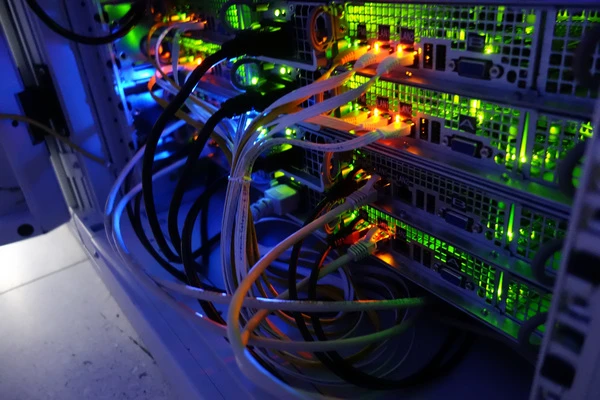 Serverrack mit bunten LEDs, Netzwerkkabeln und Steckmodulen, hell beleuchtet in Blau, Grün und Orange.