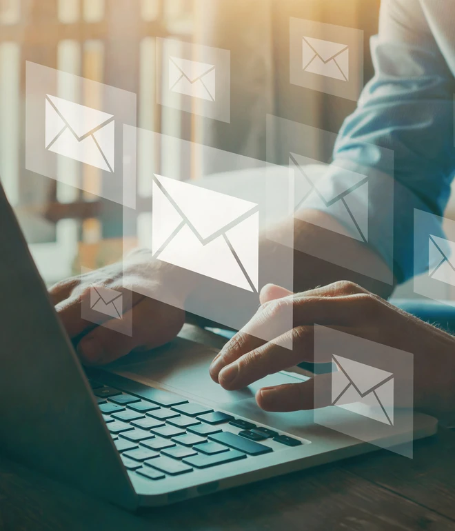 Person tippt auf Laptop, umgeben von schwebenden E-Mail-Symbolen.