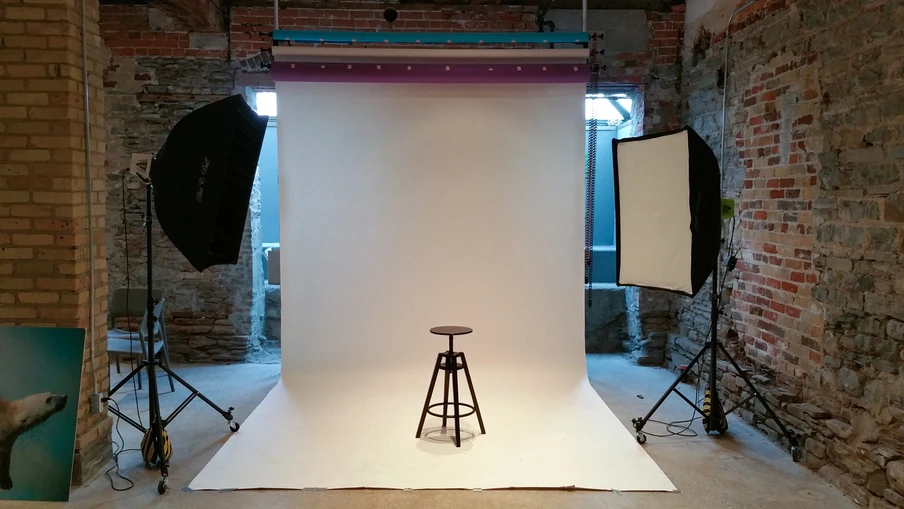 Fotostudio mit weißem Papierhintergrund, mittig Holzhocker; links und rechts Licht mit Softboxen, Ziegelwand sichtbar.
