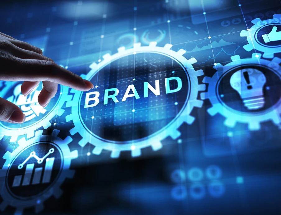 Eine Hand berührt eine holografische Anordnung blauer Zahnräder, im Zentrum steht das Wort BRAND.