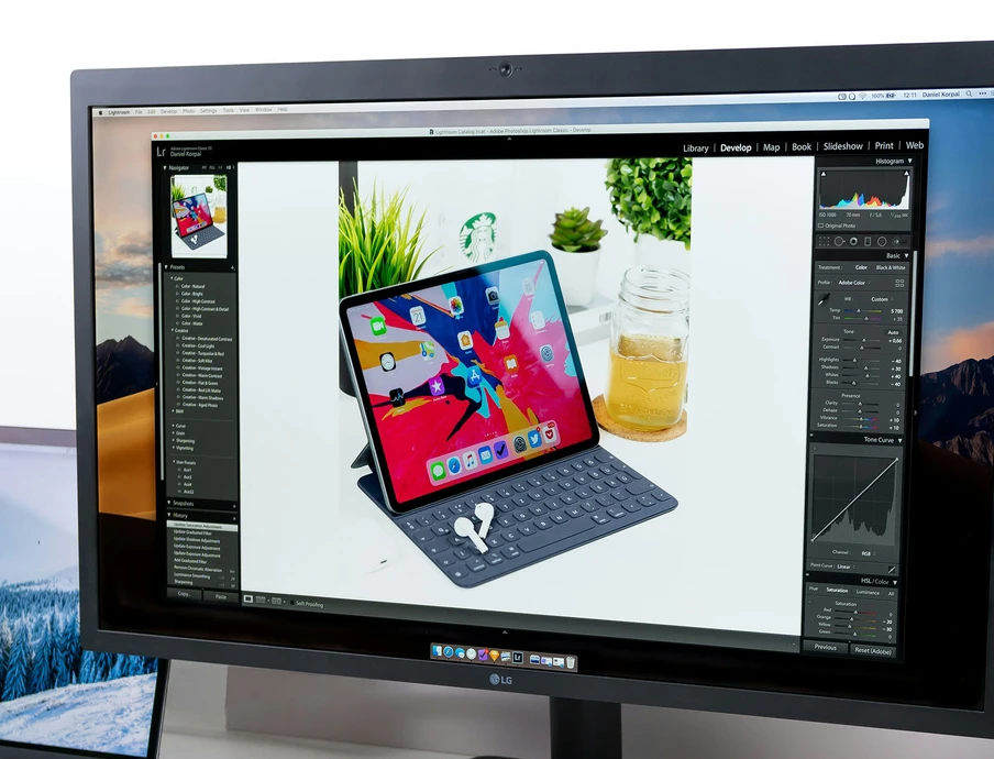 Großer Monitor mit geöffneter Bildbearbeitung; ein Tablet auf Tastaturhülle mit Stift, umgeben von Pflanzen