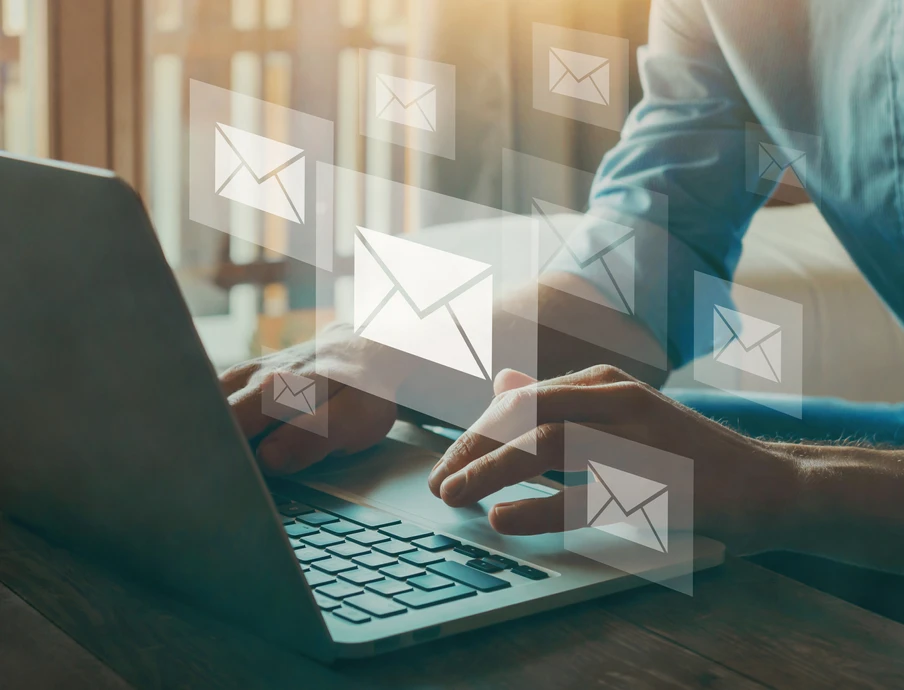 Person tippt auf Laptop, umgeben von schwebenden E-Mail-Symbolen.