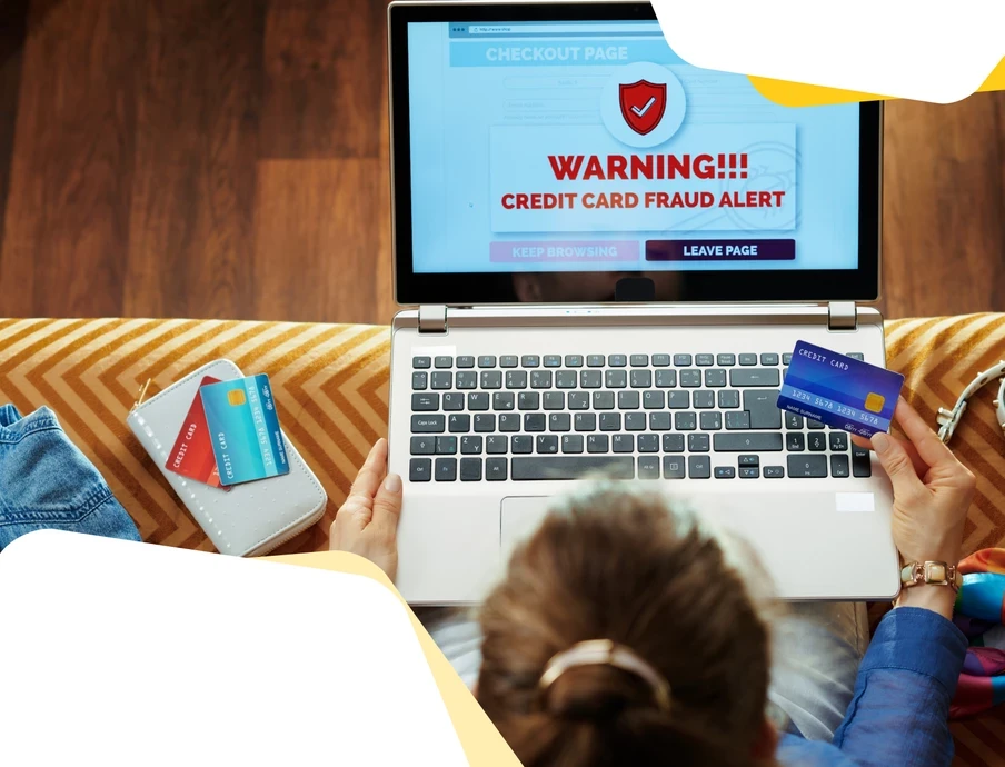 Laptop zeigt Warnhinweis Kreditkartenbetrug; zwei Hände halten Kreditkarten, links liegt eine Brieftasche mit Karten.