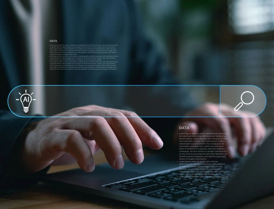 Person tippt auf Laptop; holografische blaue UI-Leiste mit Suchsymbol, AI-Icon und Textblöcken.