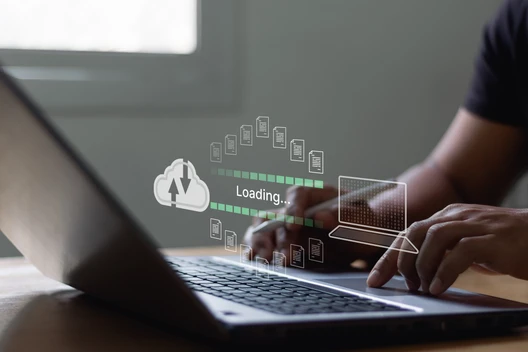 Person tippt auf Laptop; transparente Overlay-Grafik zeigt Ladebalken, Wolke mit Pfeil und App-Icons.