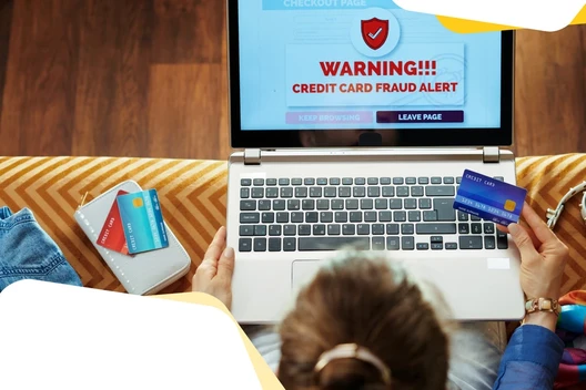 Laptop zeigt Warnhinweis Kreditkartenbetrug; zwei Hände halten Kreditkarten, links liegt eine Brieftasche mit Karten.