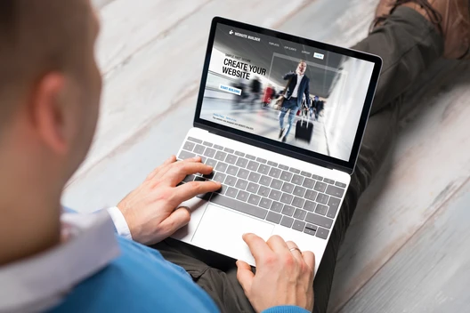 Person sitzt mit Laptop auf Holzboden; Laptopbildschirm zeigt Website-Entwurf mit dem Text Create Your Website.